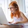 A young girl with ginger hair and glasses is working intently on a laptop