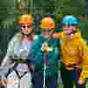 Three young people are huddled together at an Usher Kids UK event. They're wearing safety helmets and harnesses about to take part in a daring activity. They are all looking excited about what's. The image was provided by Usher Kids UK from an event that took place in 2024