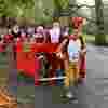 A group of runners running along a road in Santa suits, in the front is a man wearing a reindeer costume, pulling a cardboard sleigh with three santas inside it