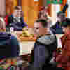 A group of young people with vision impairment taking part in a farm visit. They are sitting around a table exchanging stories and laughing. 