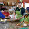 A group of young people with vision impairment on a farm visit, funded by Fight for Sight. They are standing around a counter and preparing food. 