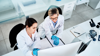 Two researchers in lab coats looking curiously at a computer.