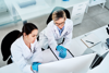 Two researchers in lab coats looking curiously at a computer.