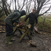 Two people sawing wood in a muddy clearing at Jamie's Farm Lewes