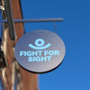 Fight for Sight hanging sign, a navy blue circle with our logo in the centre, with a blue sky behind. 